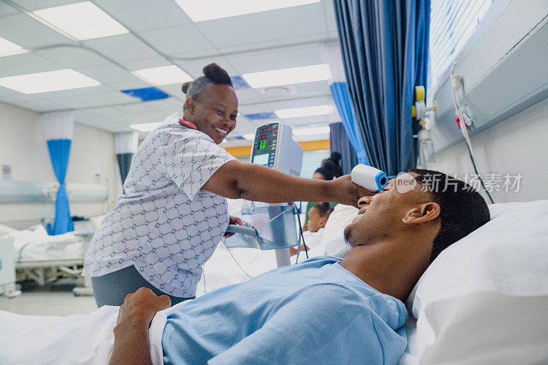 在繁忙的病房里，友善的女护士在病床上给戴着助听器的年轻男性测体温