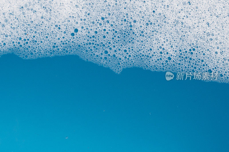 洗涤剂在水中起泡沫。蓝色背景，肥皂色