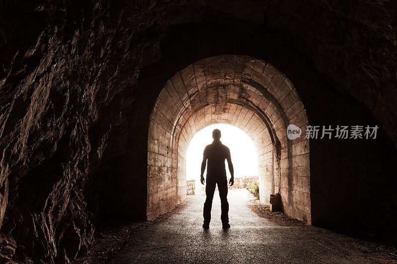 一个年轻人站在黑暗的混凝土隧道里