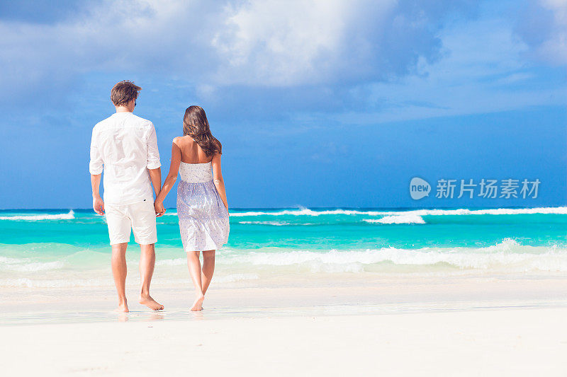 年轻幸福的夫妇穿着白色衣服在热带海滩。度蜜月