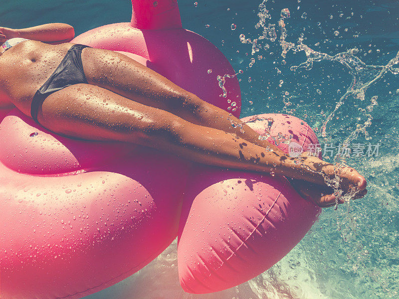 一个女人在游泳池里漂浮在粉红色的充气上。