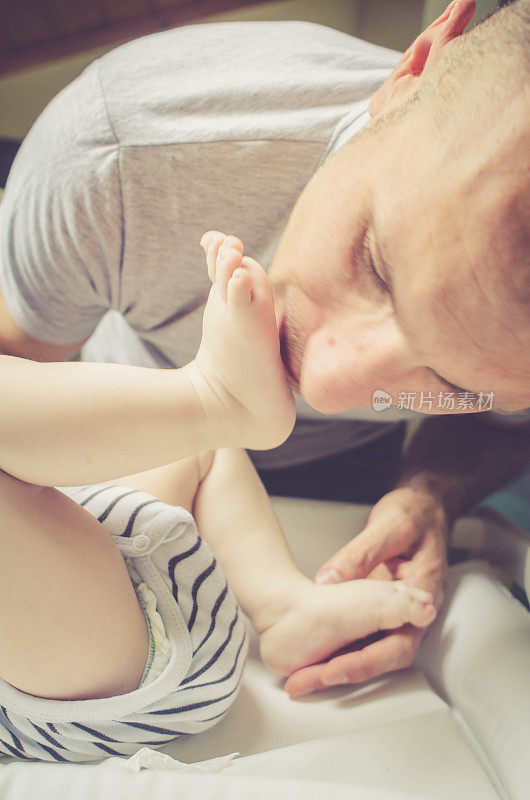顽皮的爸爸给宝宝换尿布，亲吻宝宝的脚