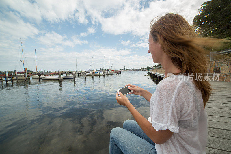 年轻女子在码头上休息，在手机上发短信