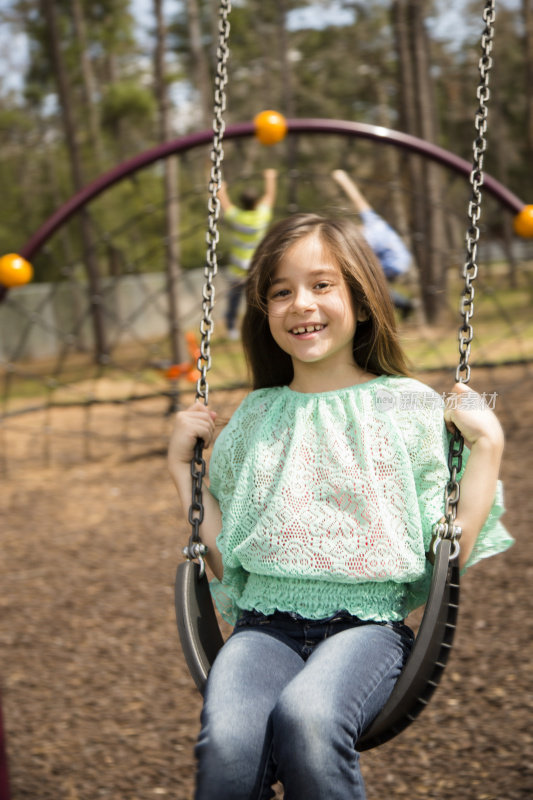 快乐的小学女孩在公园或学校操场荡秋千。