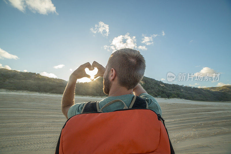 在日落的海滩上的旅行者做心形的手指框架