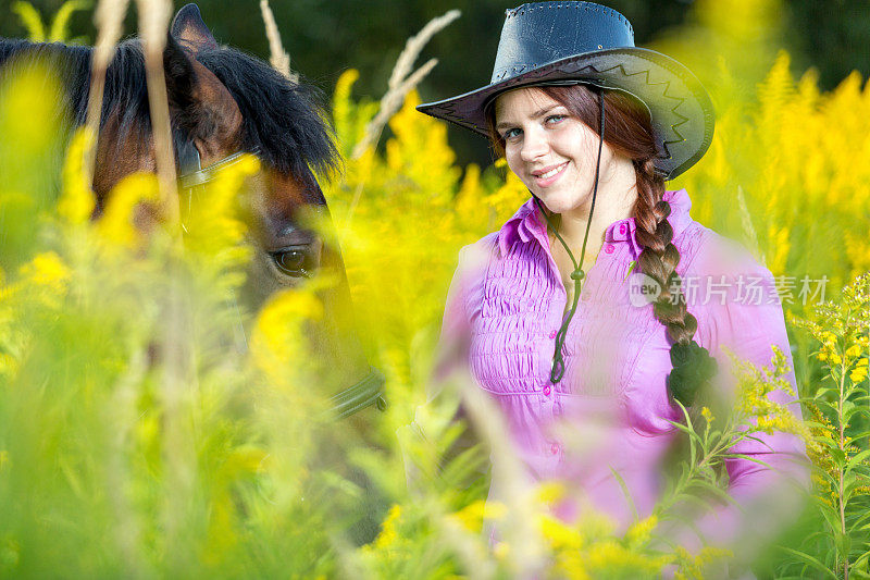 美丽的女牛仔和马在绿草中