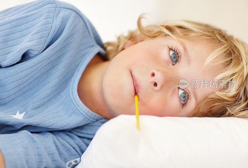 一个生病的男孩躺在床上，嘴里含着温度计