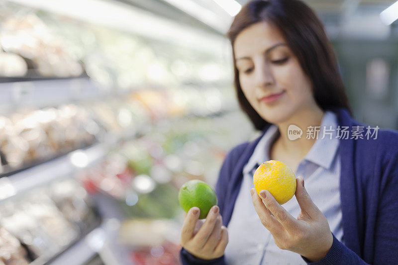 在杂货店农产品通道里比较柠檬和酸橙的女人