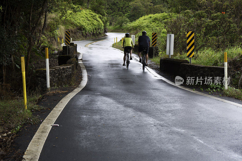 两个骑自行车的人在潮湿的乡村道路上