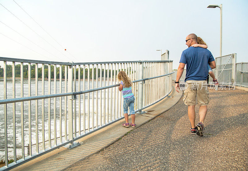 父亲和女儿们走过大坝上的桥