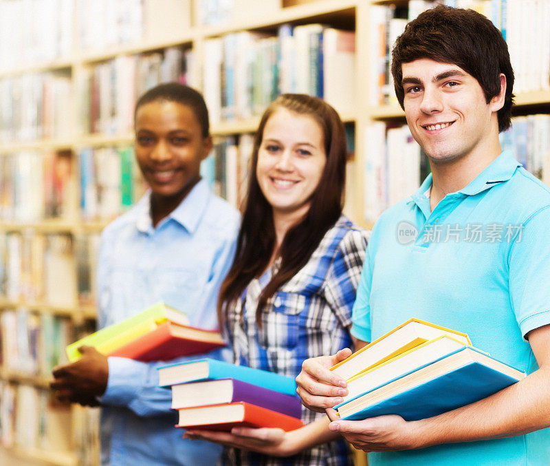 三个面带微笑的学生，每个人都拿着书，在校园图书馆里