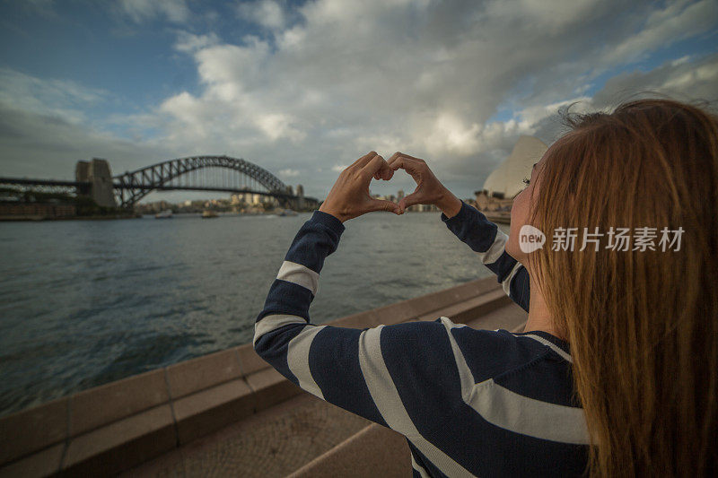 一名年轻女子在悉尼港制作心形手指架