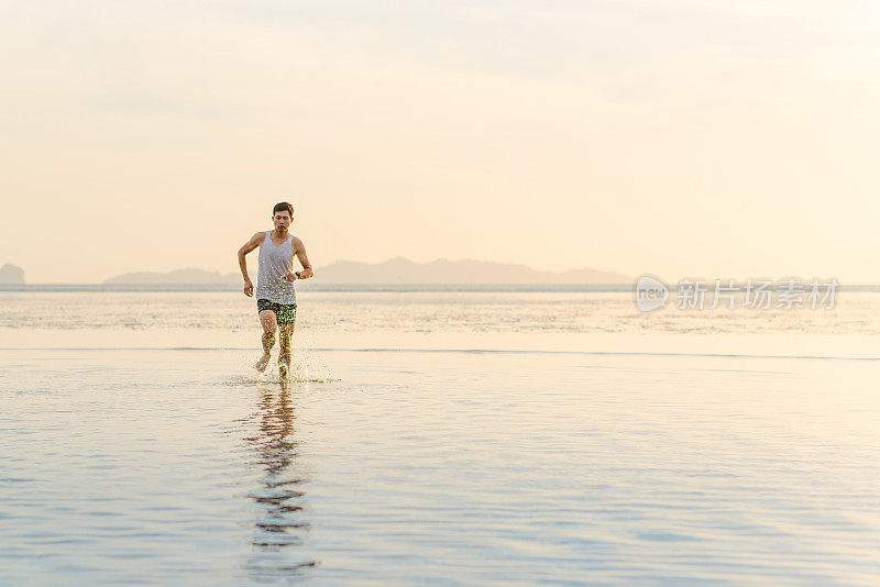 年轻的亚洲男子在海滩上奔跑，夕阳为背景