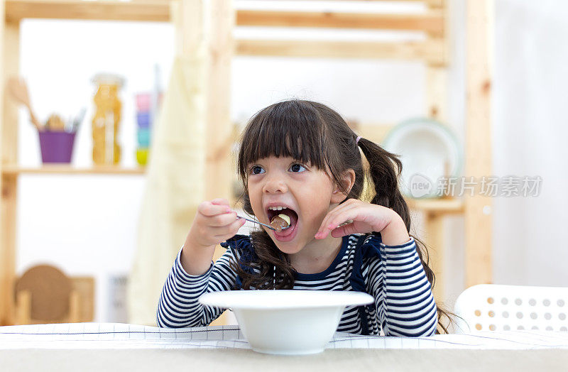 可爱的小女孩在厨房里喝牛奶吃麦片