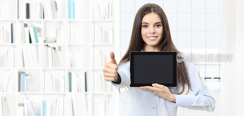 微笑的女人竖起大拇指，展示图书馆背景上的数字平板电脑