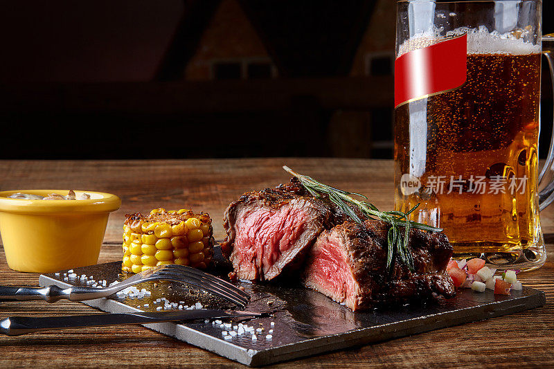 烤里脊牛排，烤牛肉和蘑菇酱在黑色砧板上和一杯啤酒在木桌上