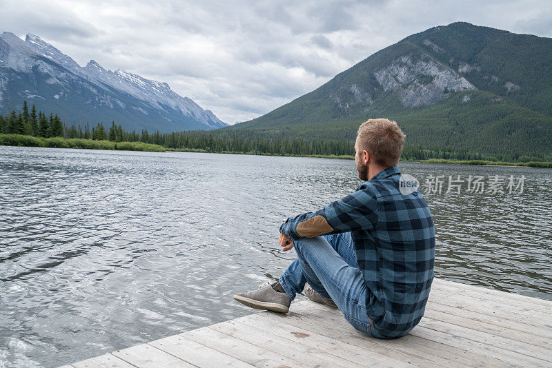 年轻男子在湖码头上看风景