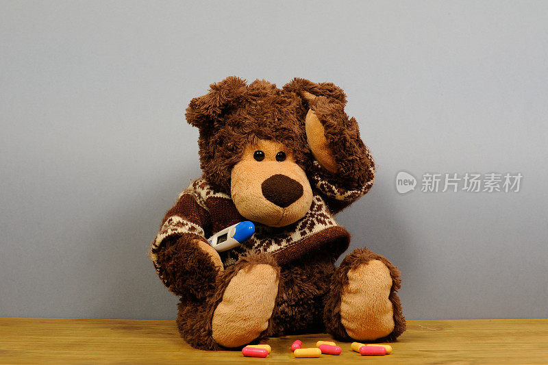 灰色背景上带温度计的泰迪熊。发烧和头痛的人。熊玩具病了。