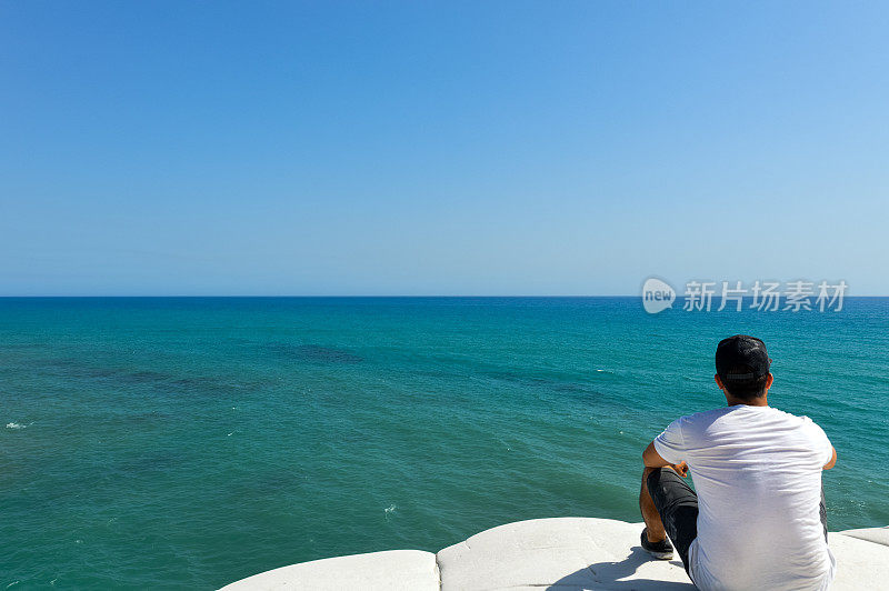 年轻人坐在悬崖上看热带海洋