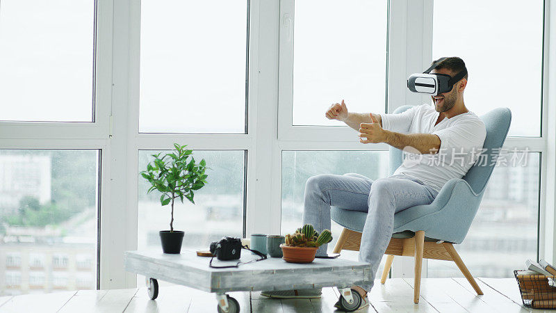有VR经验的年轻人坐在阳台的椅子上，用虚拟现实头盔玩电脑赛车游戏