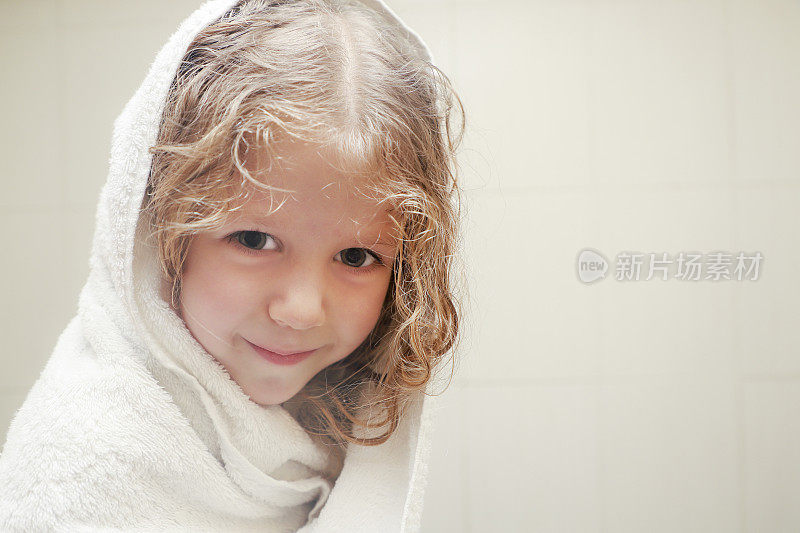 洗完澡后，小卷毛女孩在浴室里裹着毛巾。