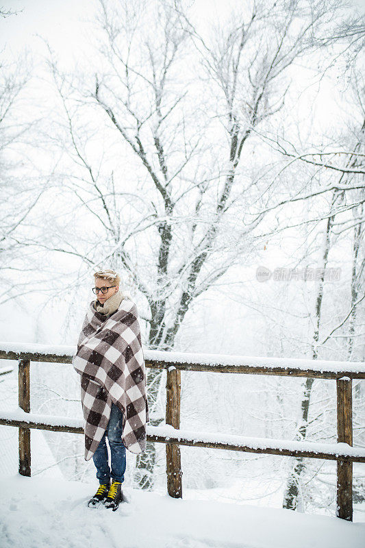 在冬天的森林里，年轻的金发女子用毯子盖着自己。