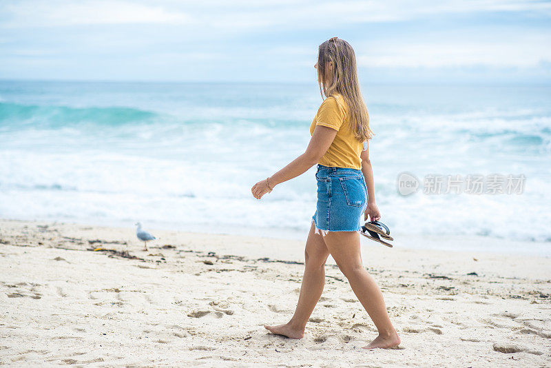 年轻女子赤脚在海边散步