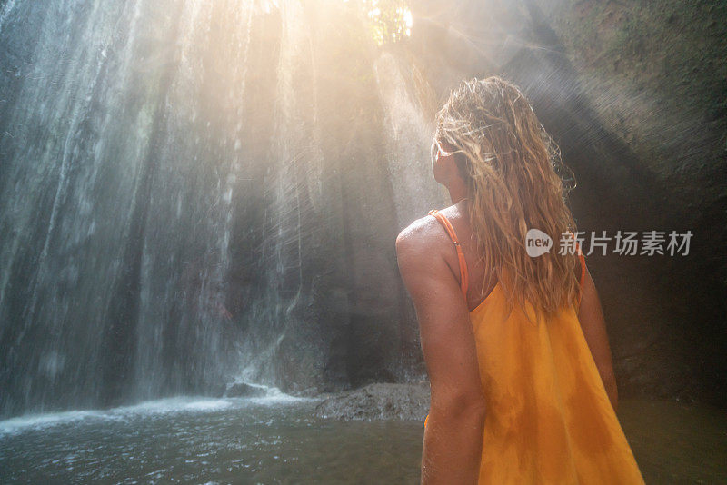 穿着黄色衣服的女孩站在热带雨林的洞穴里，仰望着从岩石上射下来的壮观的阳光。人们旅行的奇妙欲望自然的概念