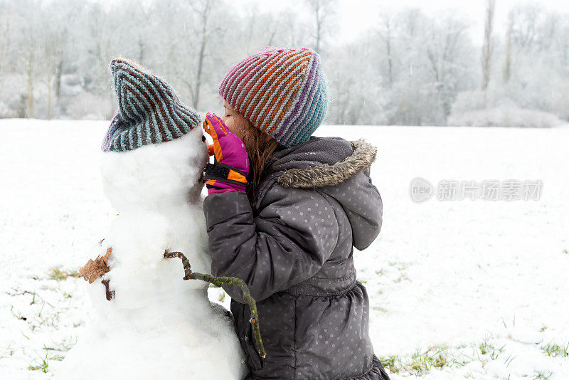 小女孩在玩雪人——它正在吃雪人的胡萝卜鼻子