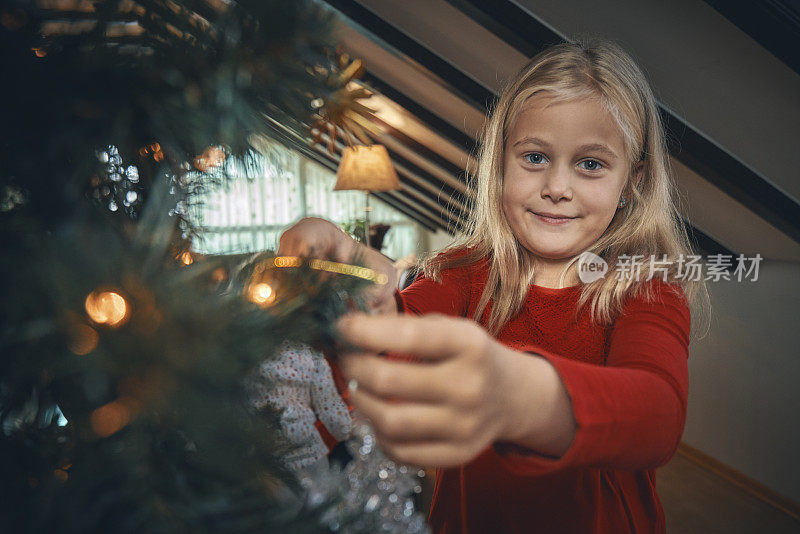 小女孩用装饰品和圣诞灯装饰圣诞树