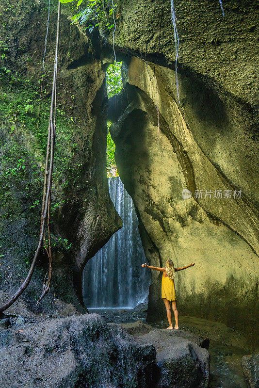 在巴厘岛的热带雨林中，旅行的年轻女子张开双臂拥抱大自然的美丽。人们以自然为旅游理念。