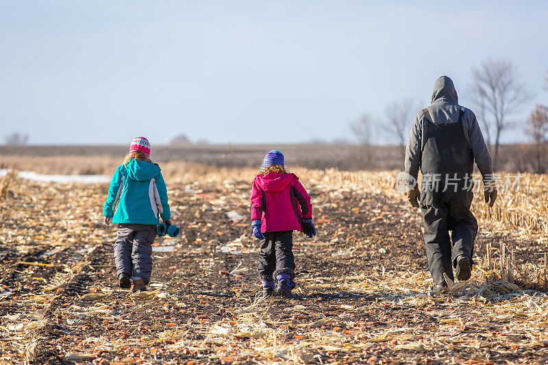 爷爷和孙女在冬天走过收获的玉米地