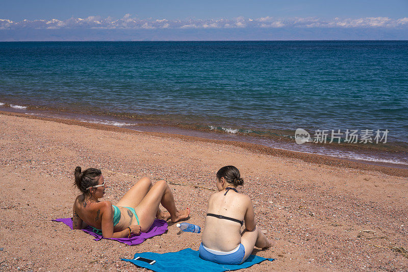 两名游客在吉尔吉斯斯坦伊西库尔湖的海滩上休息