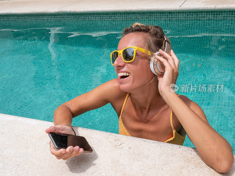 快乐的女人戴着耳机在游泳池里听音乐