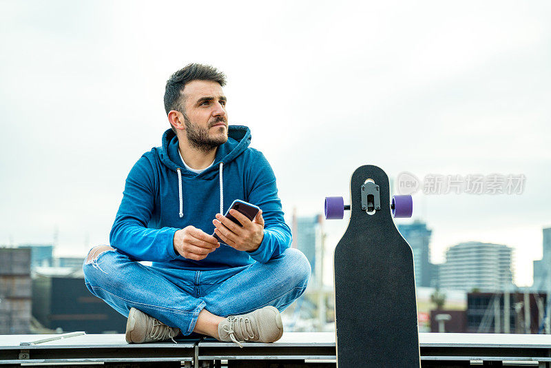 一名男子坐在长板旁，用着智能手机