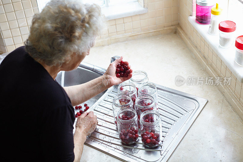 妇女准备自制樱桃蜜饯罐头在罐子冬天在她的厨房