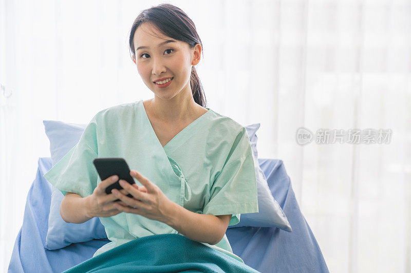亚洲妇女生病的病人躺在医院的床上使用笔记本电脑和智能手机放松时，她的病在医院恢复。