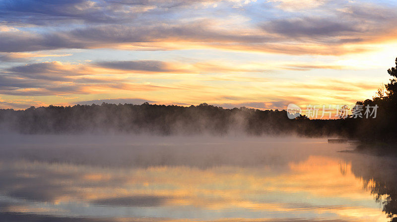 日出时，一层明亮的缕缕云覆盖在冒着热气的森林湖和码头上