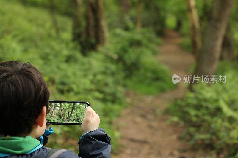 一个男孩在森林小径上用手机拍照