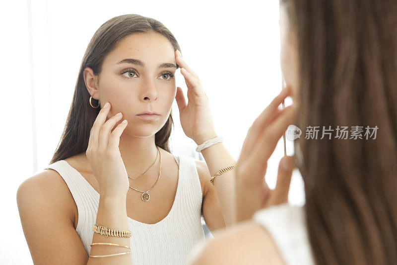 年轻女子看着她的痤疮疤痕在镜子里