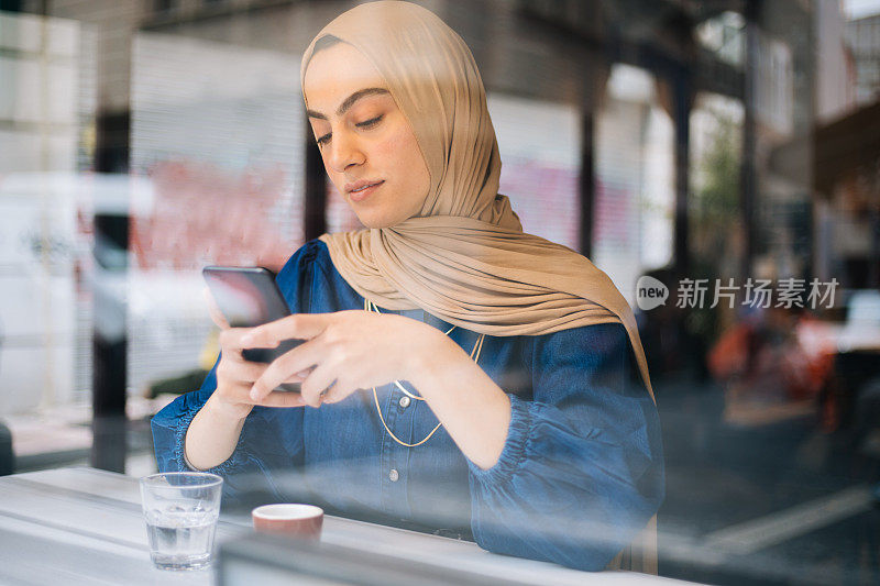 年轻的穆斯林女性在咖啡馆使用智能手机
