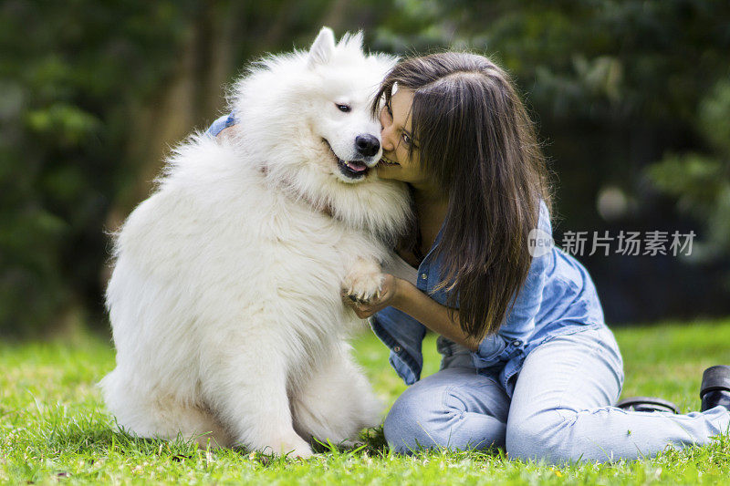 年轻女子拥抱她美丽的狗，享受一天在公园