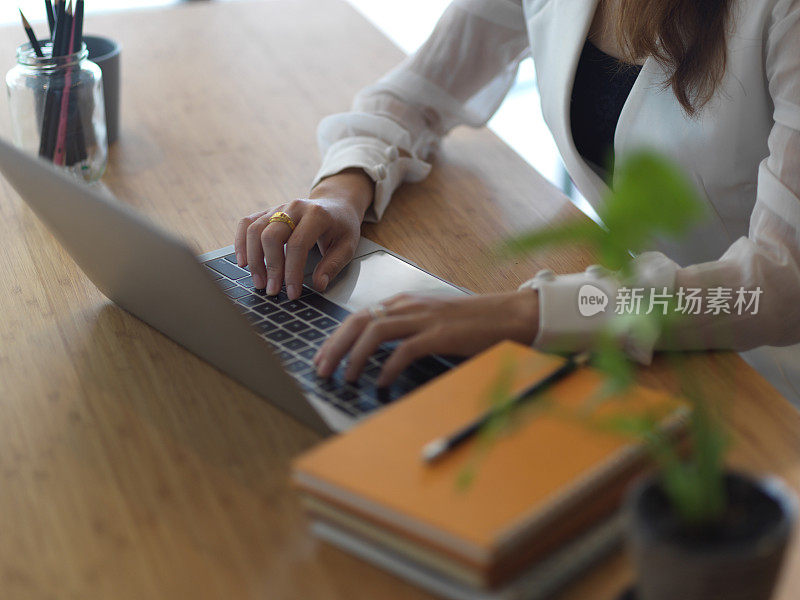 女性双手在木桌上敲击笔记本电脑键盘的镜头