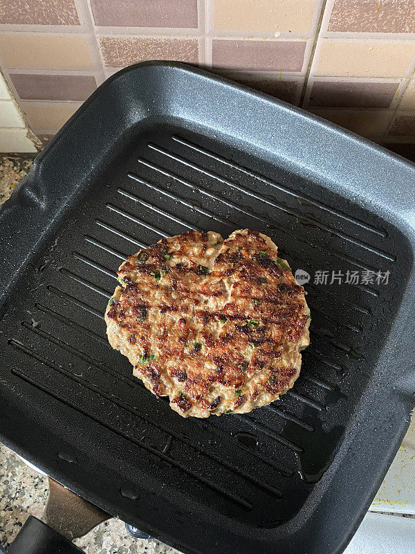 不粘锅里装着自制的牛肉汉堡肉饼，用碎肉和洋葱在煎锅上煎成，厨房场景，俯瞰