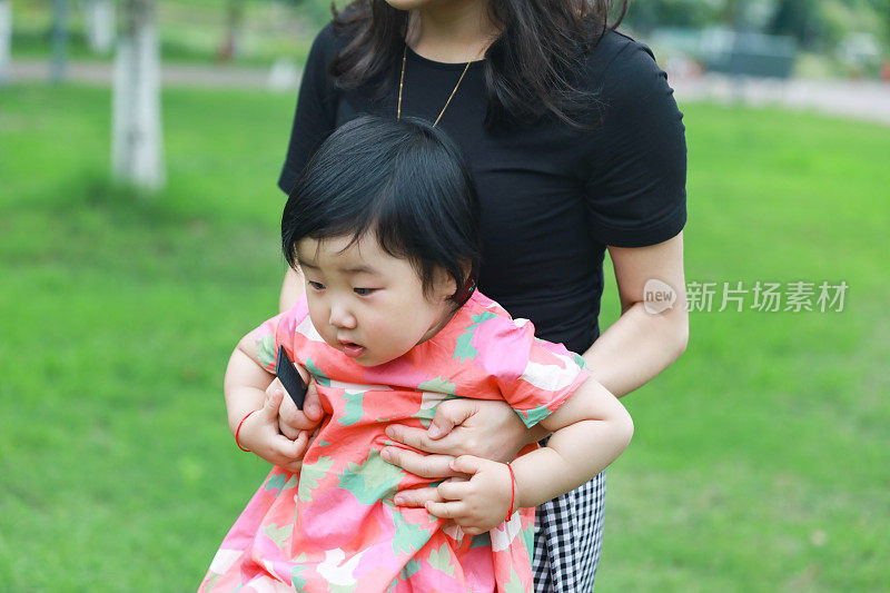 一个中国女孩抱着她的母亲在一个绿草背景的公园里
