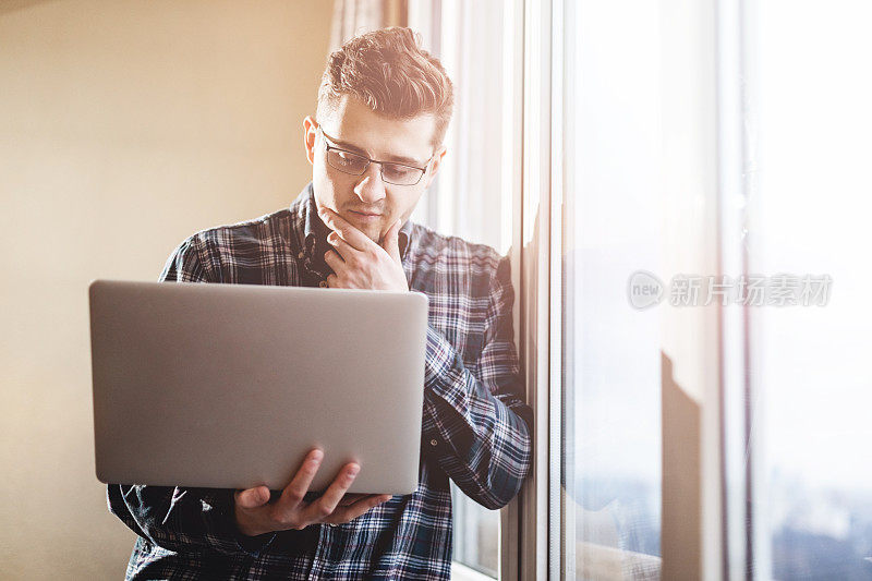 一个戴着眼镜的聪明男人的肖像。他穿着正式。他穿着衬衫、牛仔裤和运动鞋。概念照片与笔记本电脑和复制空间。