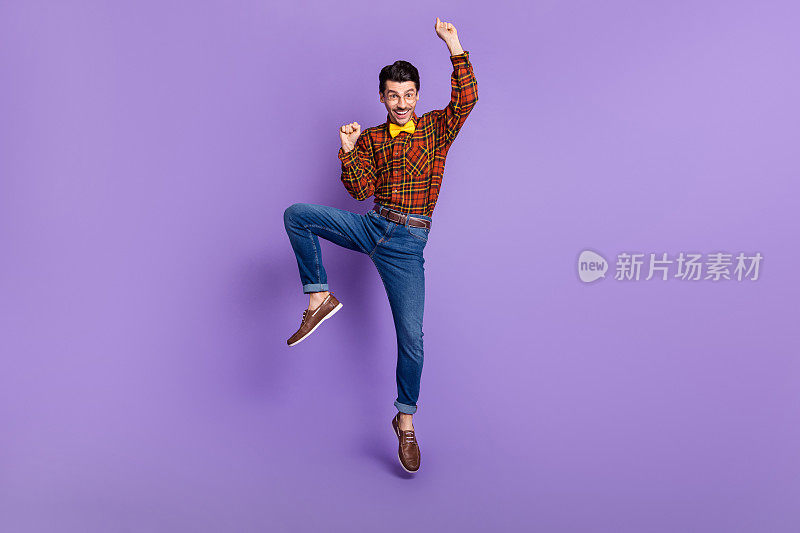 欢快的家伙跳起来，拳头，高兴穿领结，格子衬衫孤立的紫色背景