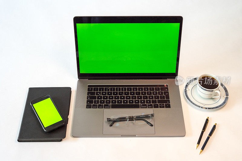 家庭办公室设置笔记本电脑绿屏智能手机绿屏记事本咖啡杯和笔都在白色桌子上横着拍照