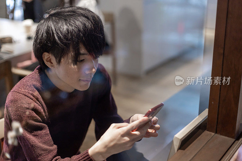 一名20多岁的男子在咖啡厅窗口操作智能手机