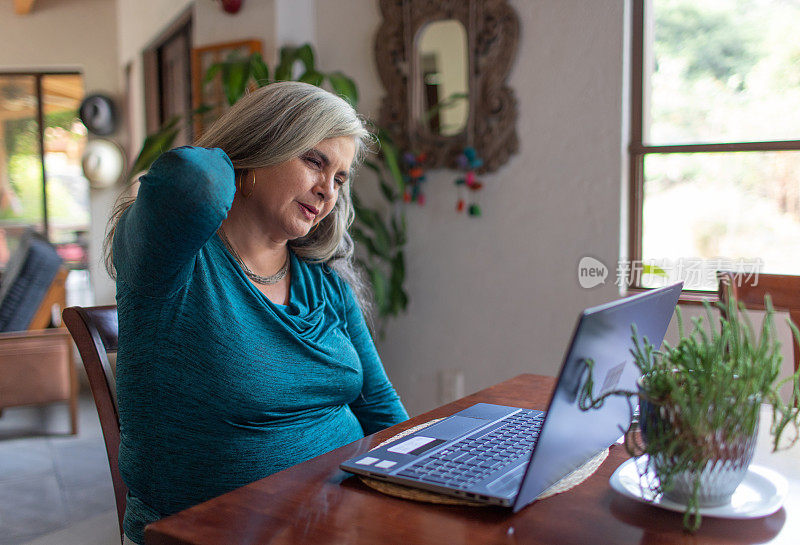 白发苍苍、脖子疼痛、工作过度的成熟女性在家使用笔记本电脑工作